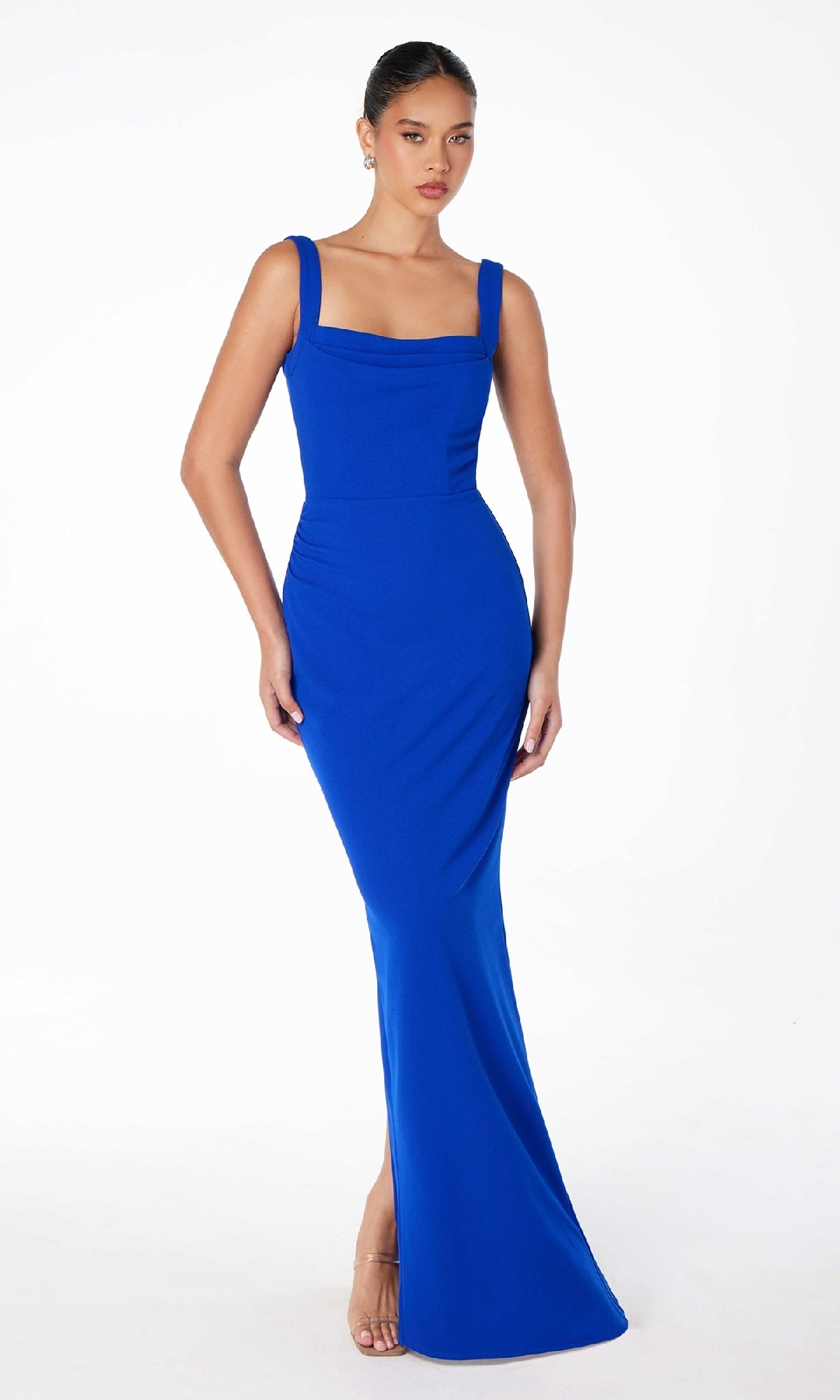 A woman stands against a plain white background wearing the Astee T3000 Square-Neck Long Prom Dress in royal blue, featuring wide straps and a fitted, floor-length silhouette, paired with nude high-heeled sandals.